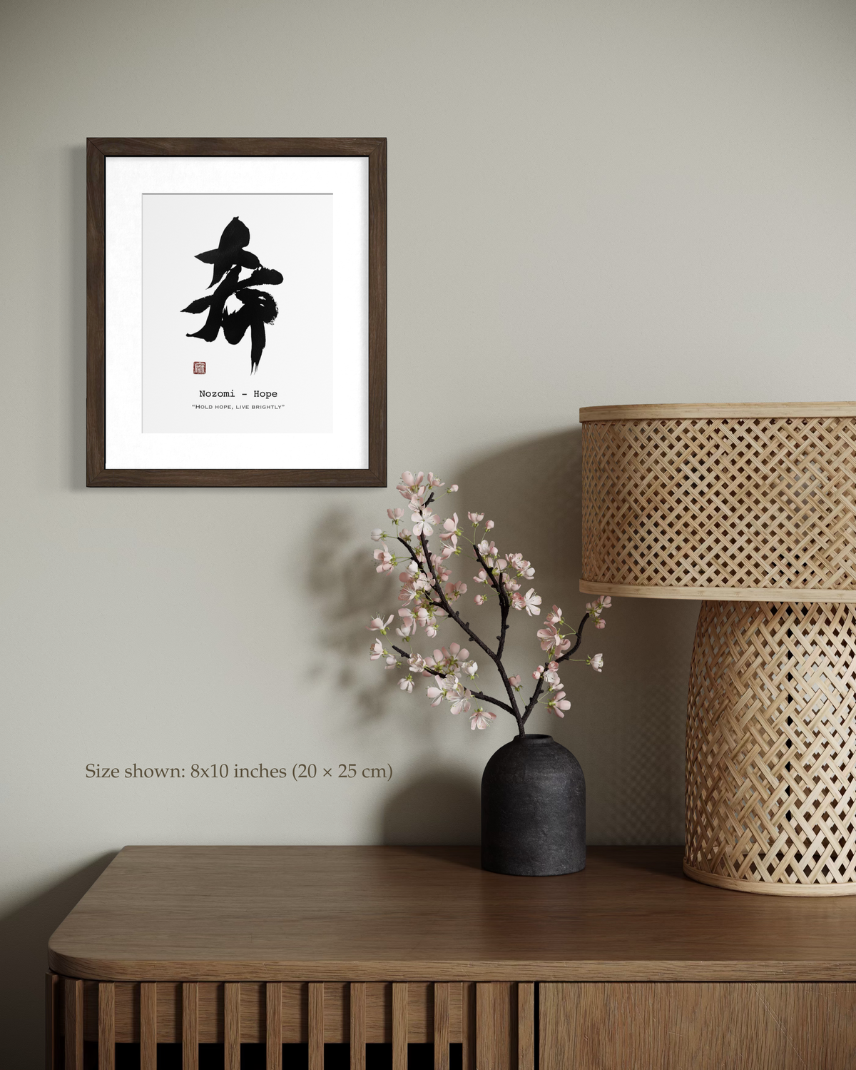 Framed calligraphy artwork on a wall above a wooden side table with a vase and lamp.