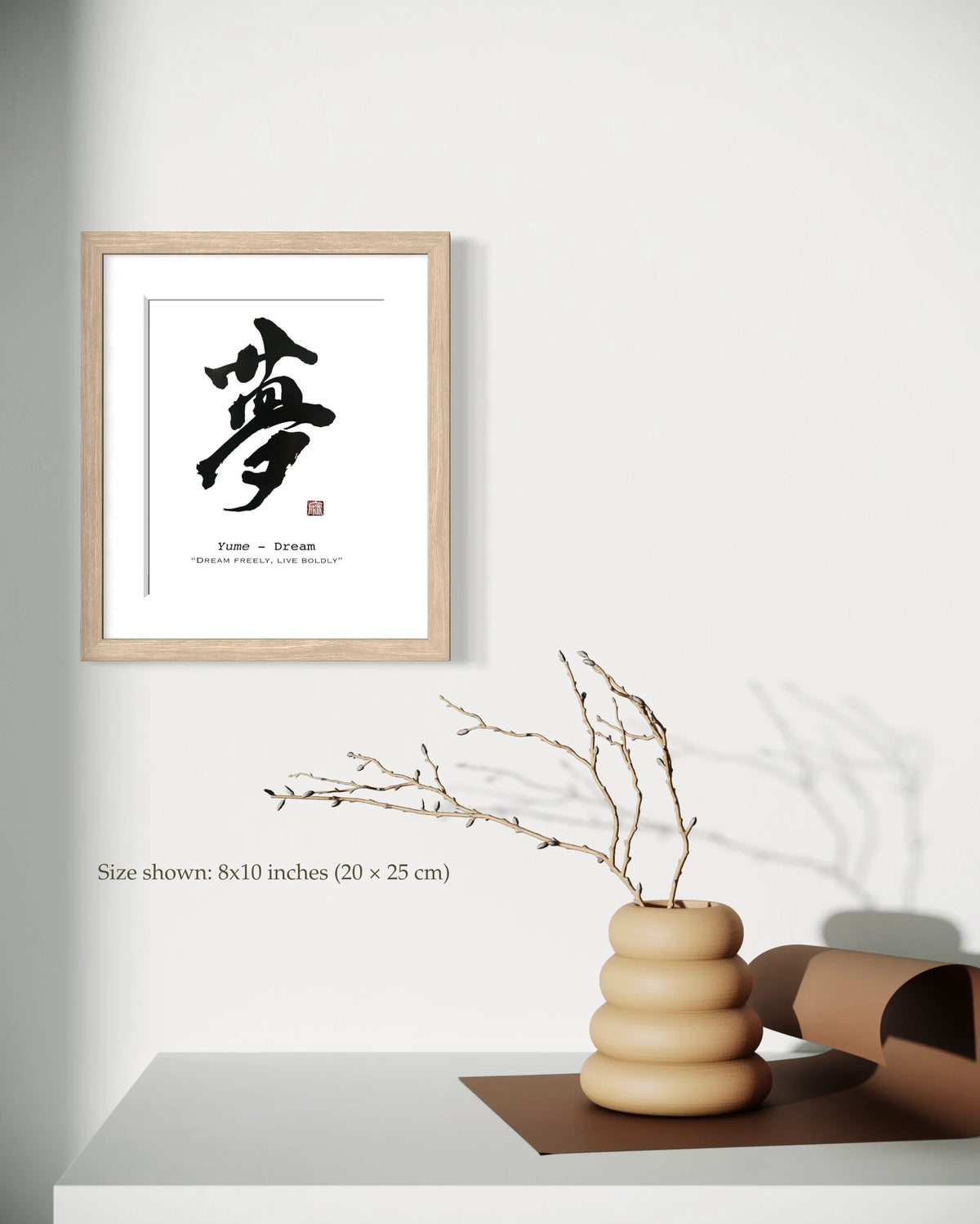 Framed artwork with a calligraphic design on a wall above a vase with branches.