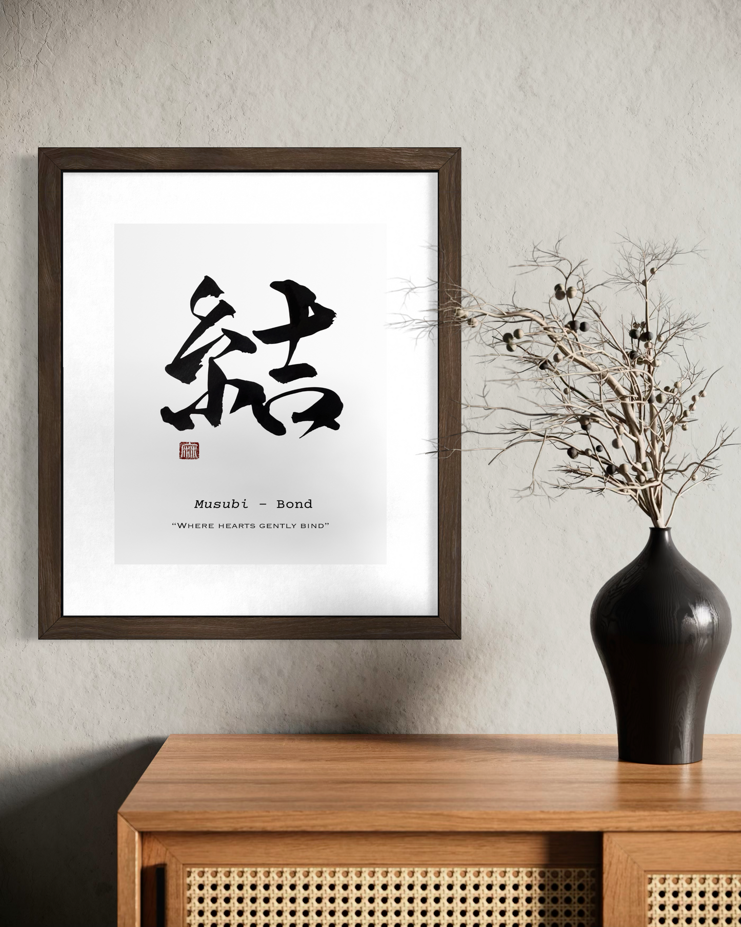 Framed artwork with Japanese calligraphy on a wall above a wooden cabinet with a black vase.