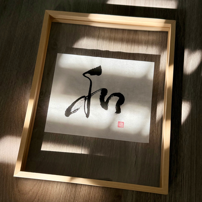 Framed minimalist Japanese calligraphy art print with black ink on white paper, sunlight on wood floor