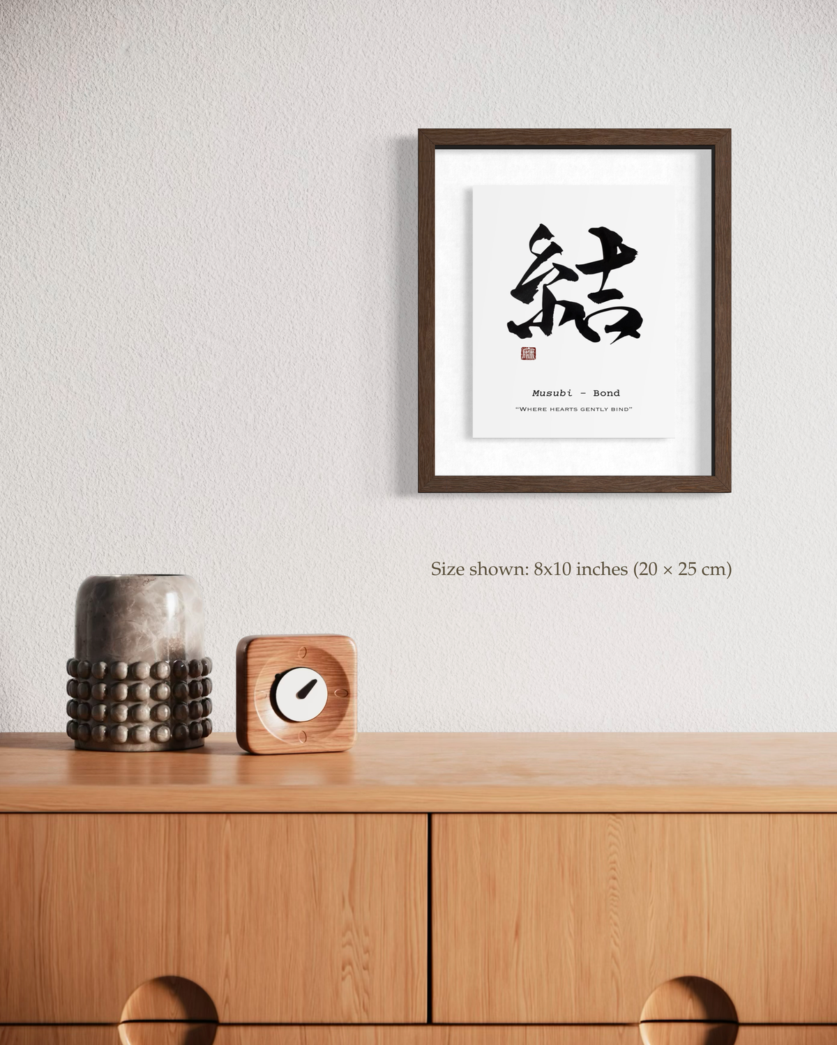 結 Musubi (Bond) calligraphy print framed 8×10 above a wooden sideboard with vase and clock