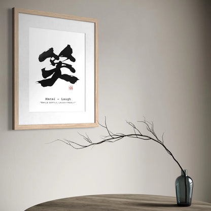 Framed artwork with black calligraphy on a gray wall above a wooden table with a vase.