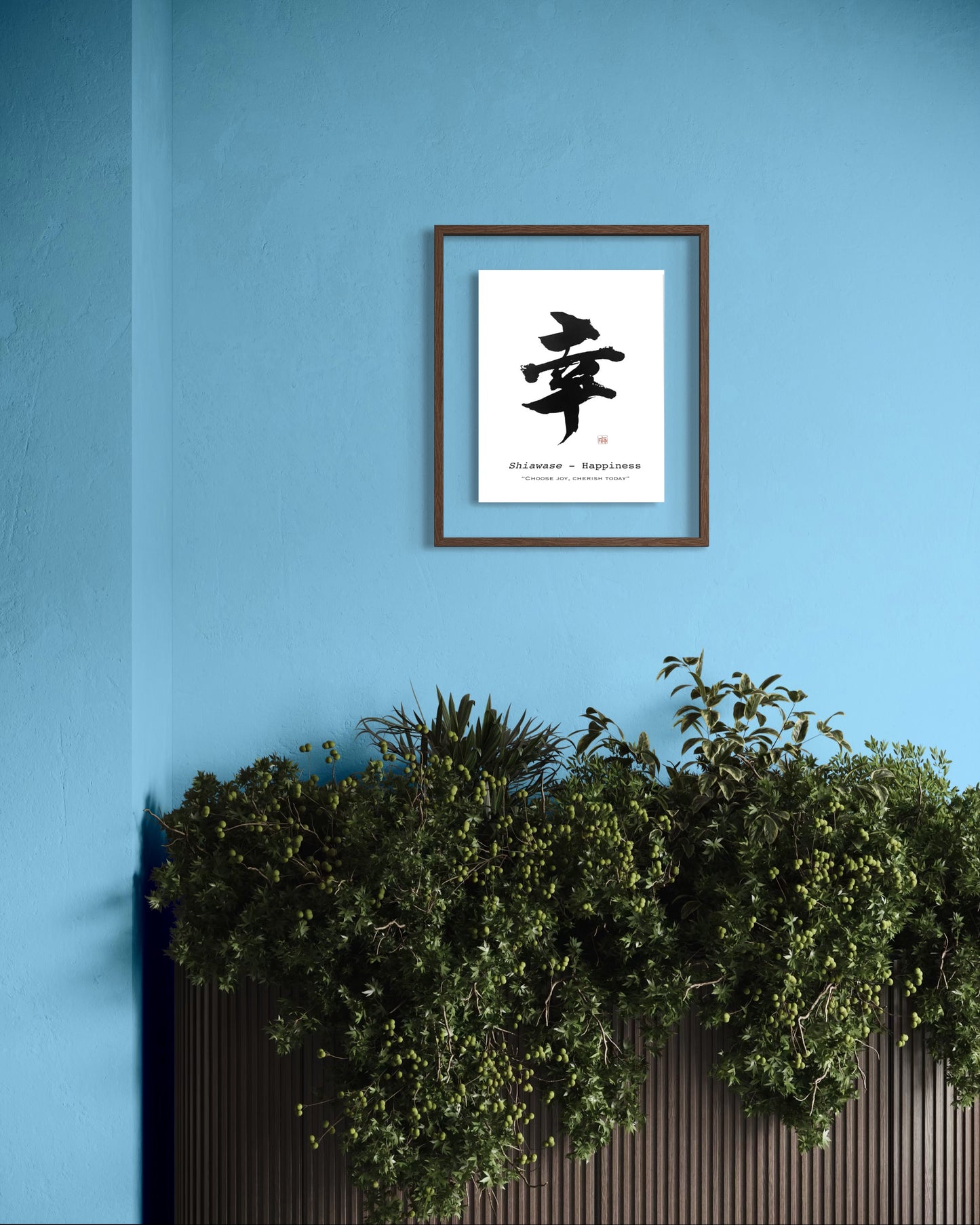 Framed japanese calligraphy artwork on a blue wall with plants below.