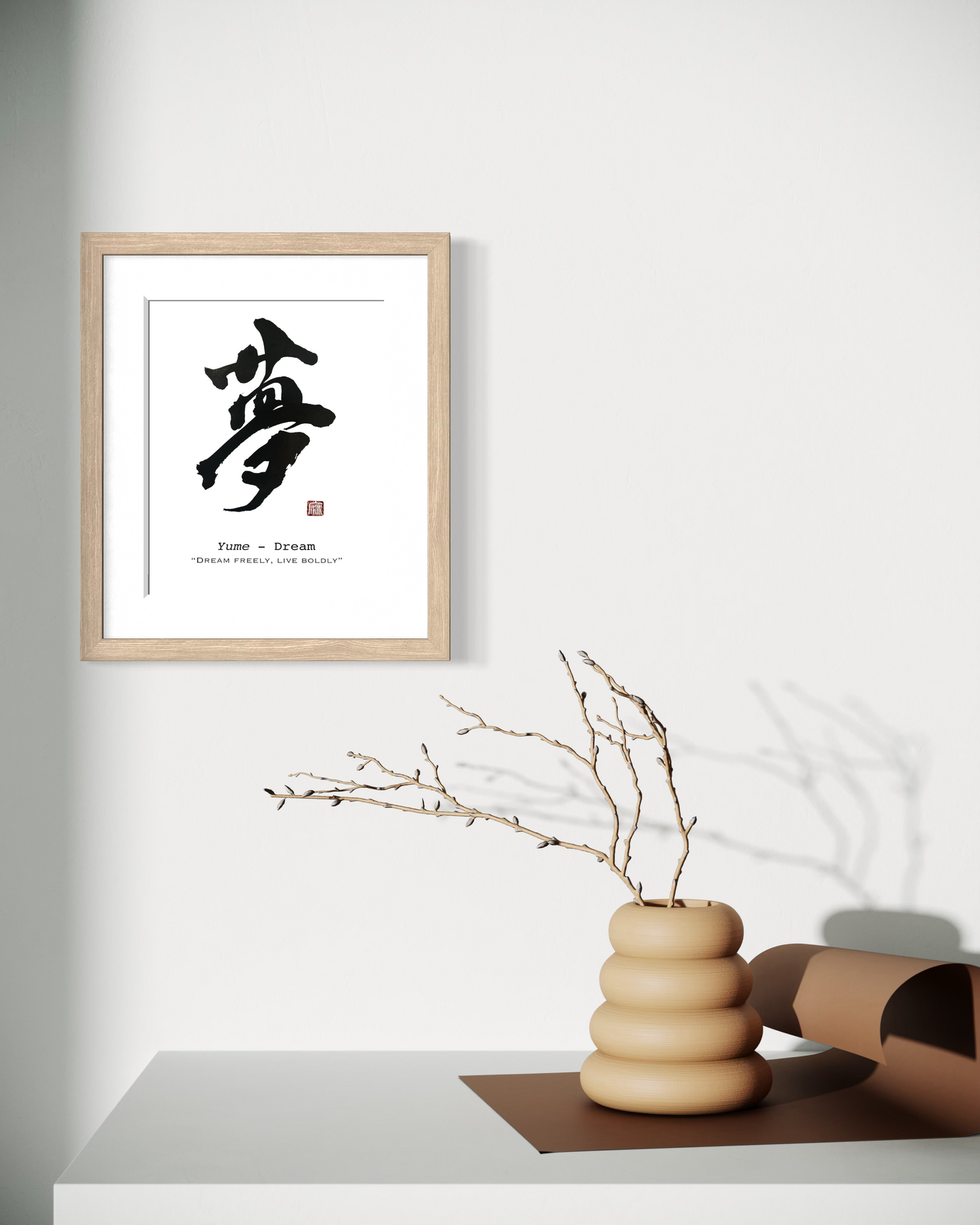 Framed artwork with a calligraphic design on a wall above a vase with branches.
